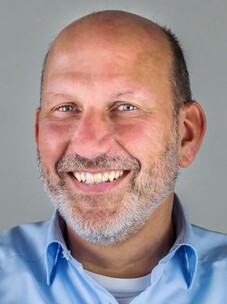 Ralph Claessen lacht freundlich in die Kamera, mit Glatze und blauem Hemd.